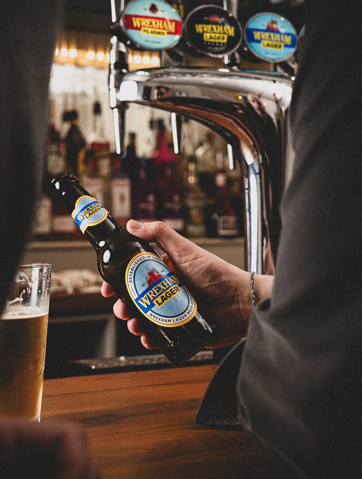 Person holding a bottle of Wrexham Lager at a bar